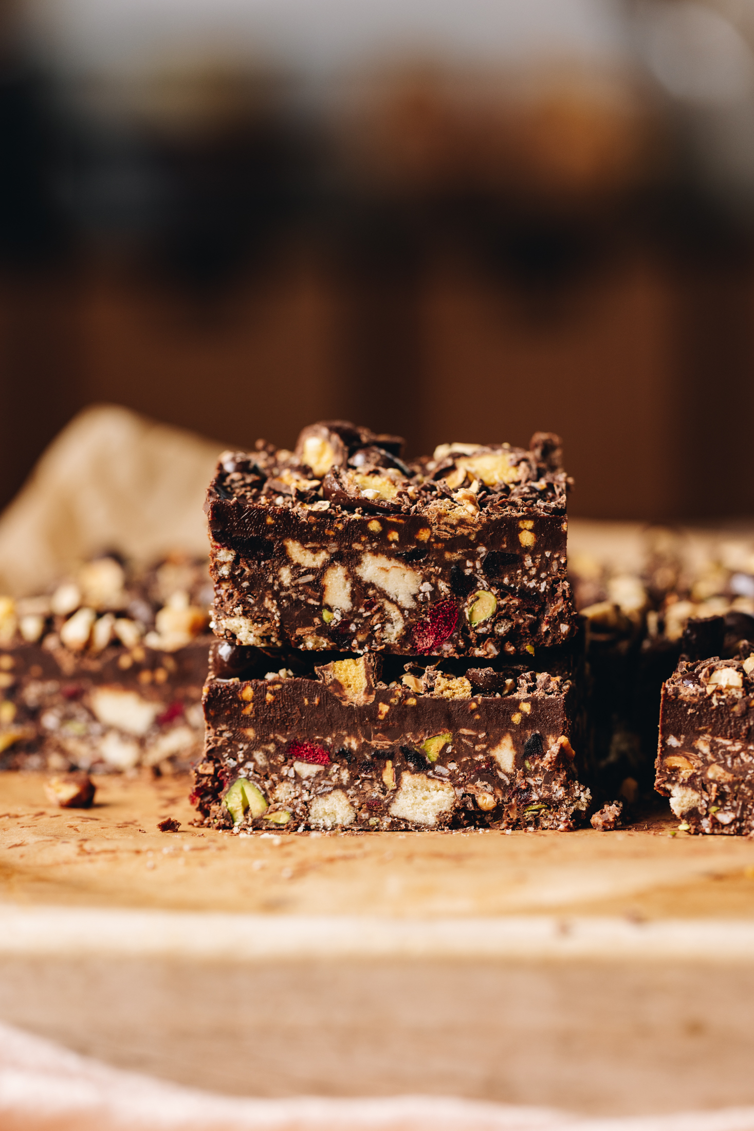 A wooden board sits on a wooden table. On top of the wooden board is pieces of no-bake hedgehog slice. Two pieces have been stacked on each other and other pieces are on either side of the stack. 