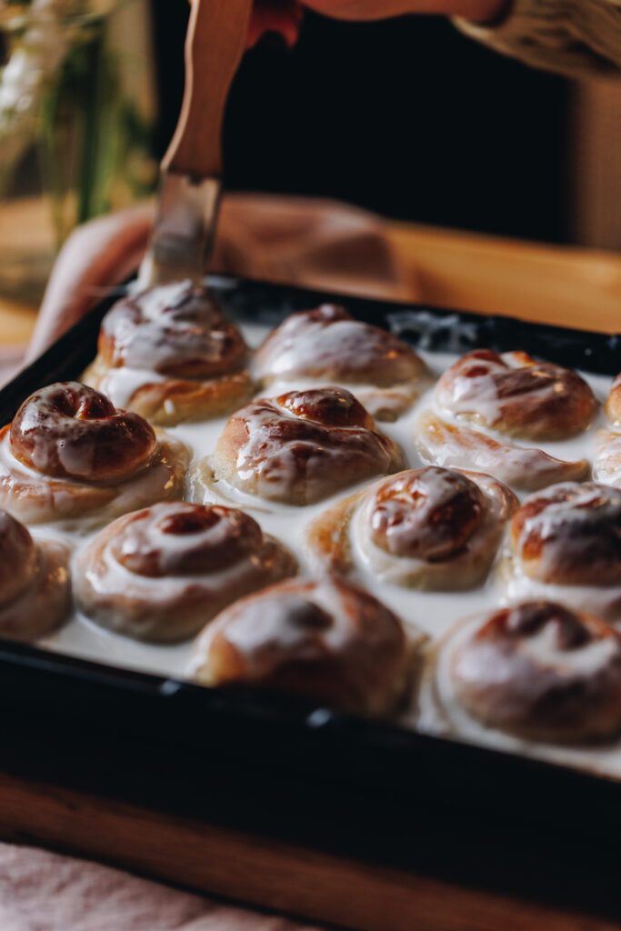 Close up of the baked Coconut Buns (Pani Popo) being bathed in coconut sauce after baking, they are in a black metal tray on a wooden table.