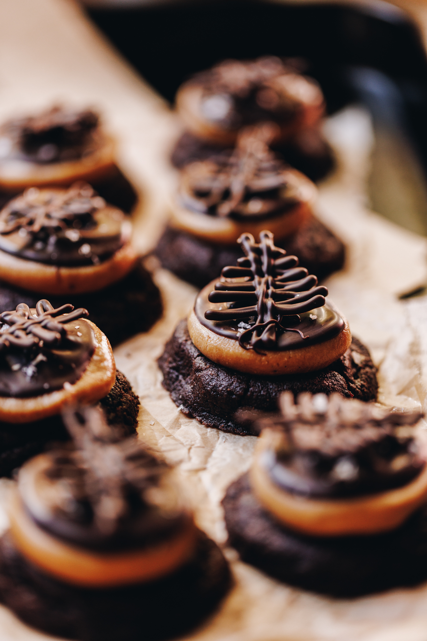 On a tray with baking sits freshly baked and decorated Buckeye Cookies. They have a chocolate cookie base with a flattened peanut butter truffle on top, melted chocolate is next and it is finished with a chocolate decoration.