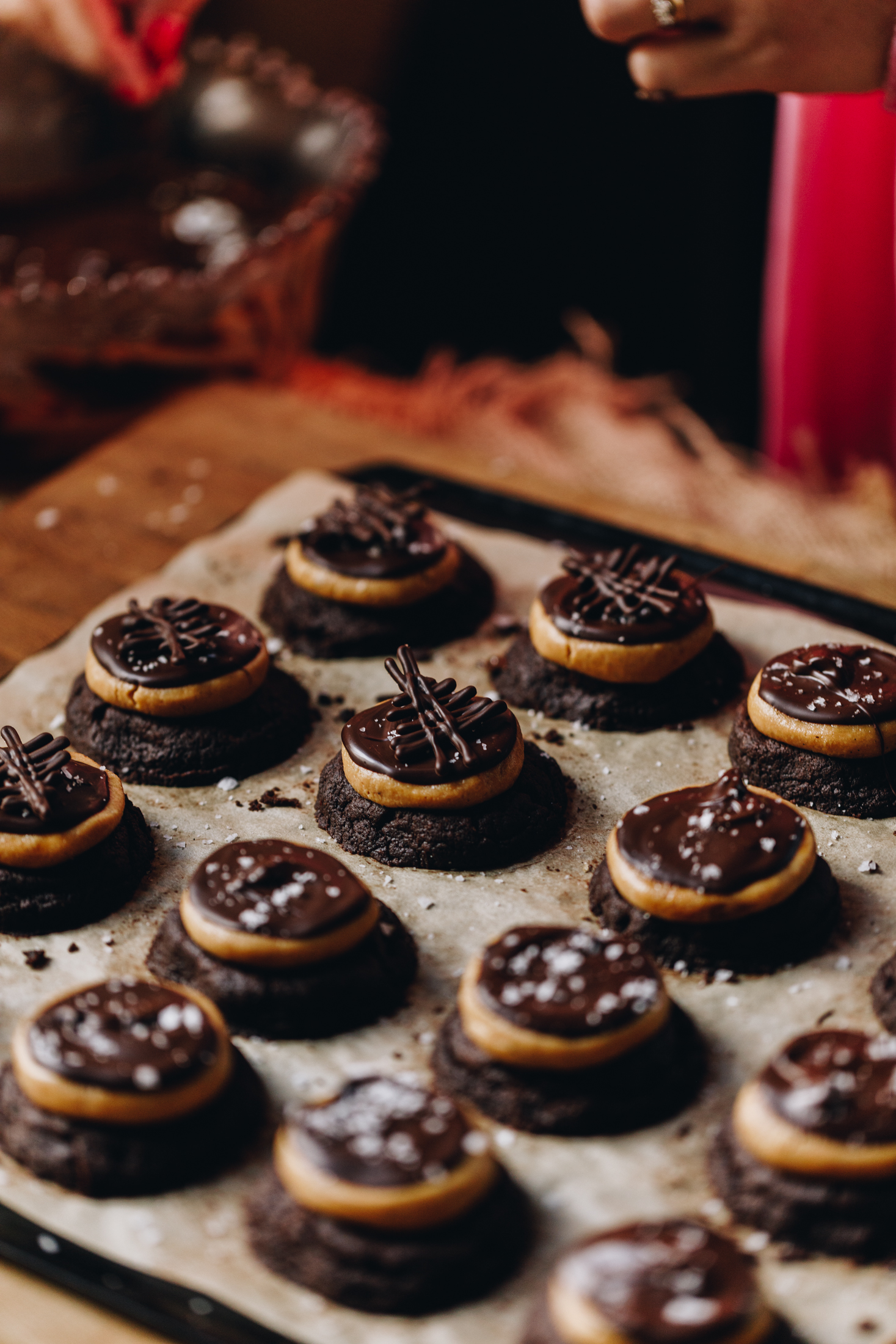 On a tray with baking sits freshly baked and decorated Buckeye Cookies. They have a chocolate cookie base with a flattened peanut butter truffle on top, melted chocolate is next and it is finished with a chocolate decoration.