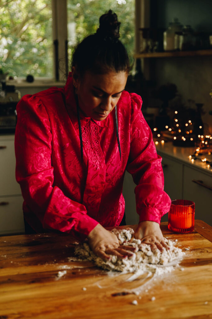 Naomi Toilalo is in her kitchen kneading the Coconut Buns (Pani Popo) dough on a wooden table with an orange candle next to her.