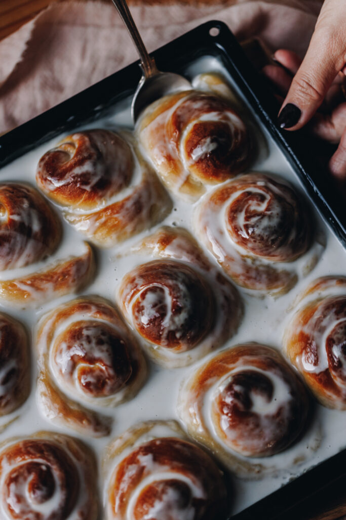 A flatlay shot showing the Freshly baked Coconut Buns (Pani Popo) in a black tray with a spoon that is starting to lift a bun out of the tray.