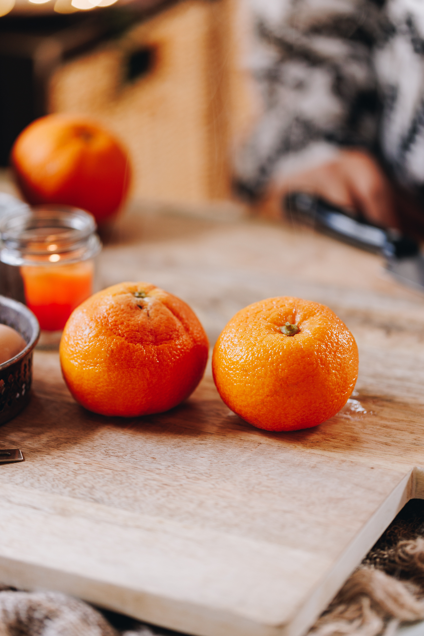 On a wooden board is two boiled oranges. A small orange candle burns in the background. 