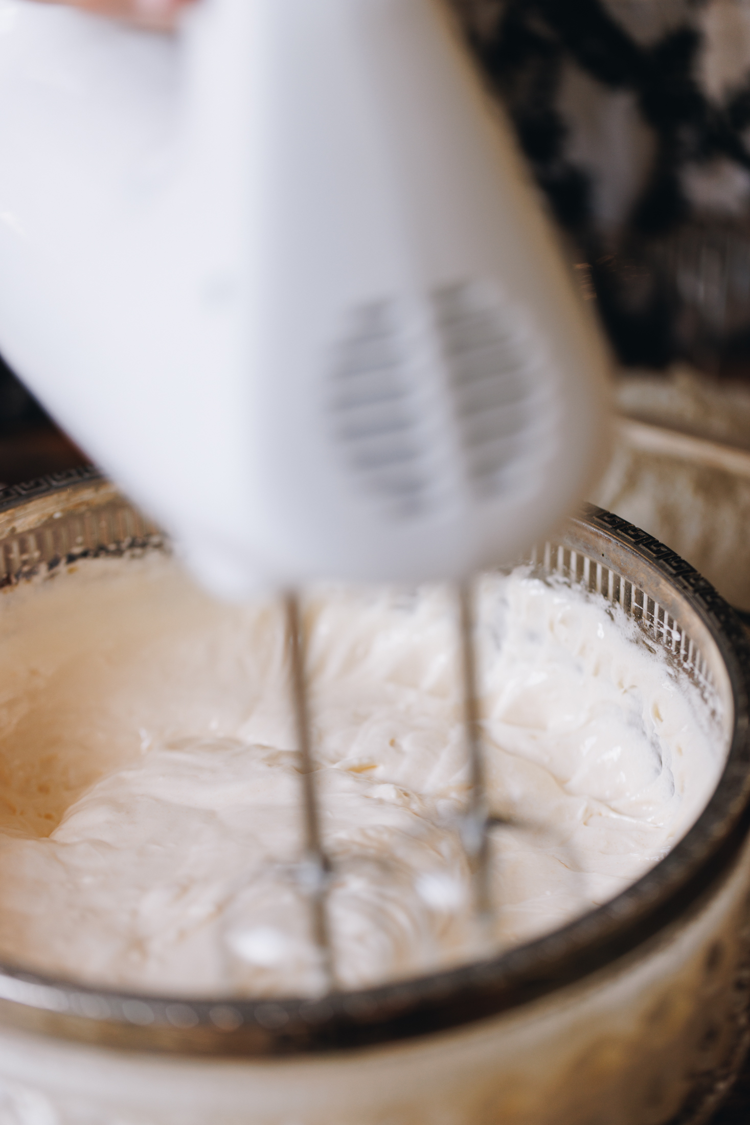 In a vintage glass bowl is eggs being whipped with a white hand beater. 