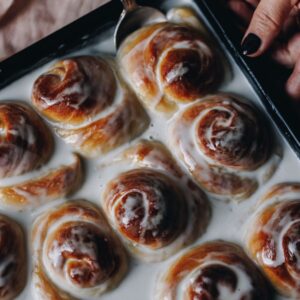 Coconut Buns (Pani Popo) have been freshly baked and one piece is being removed with a spoon, the buns are swimming in coconut sauce.