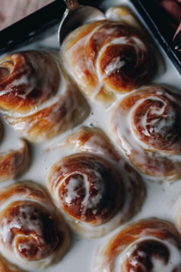 Coconut Buns (Pani Popo) have been freshly baked and one piece is being removed with a spoon, the buns are swimming in coconut sauce.