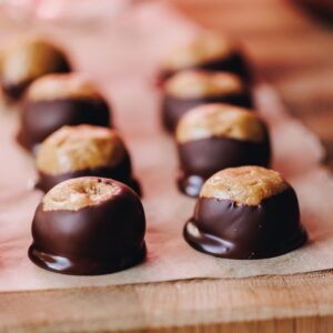 Freshly coated peanut butter buckeye truffles are on brown baking paper, on top of a wooden board.