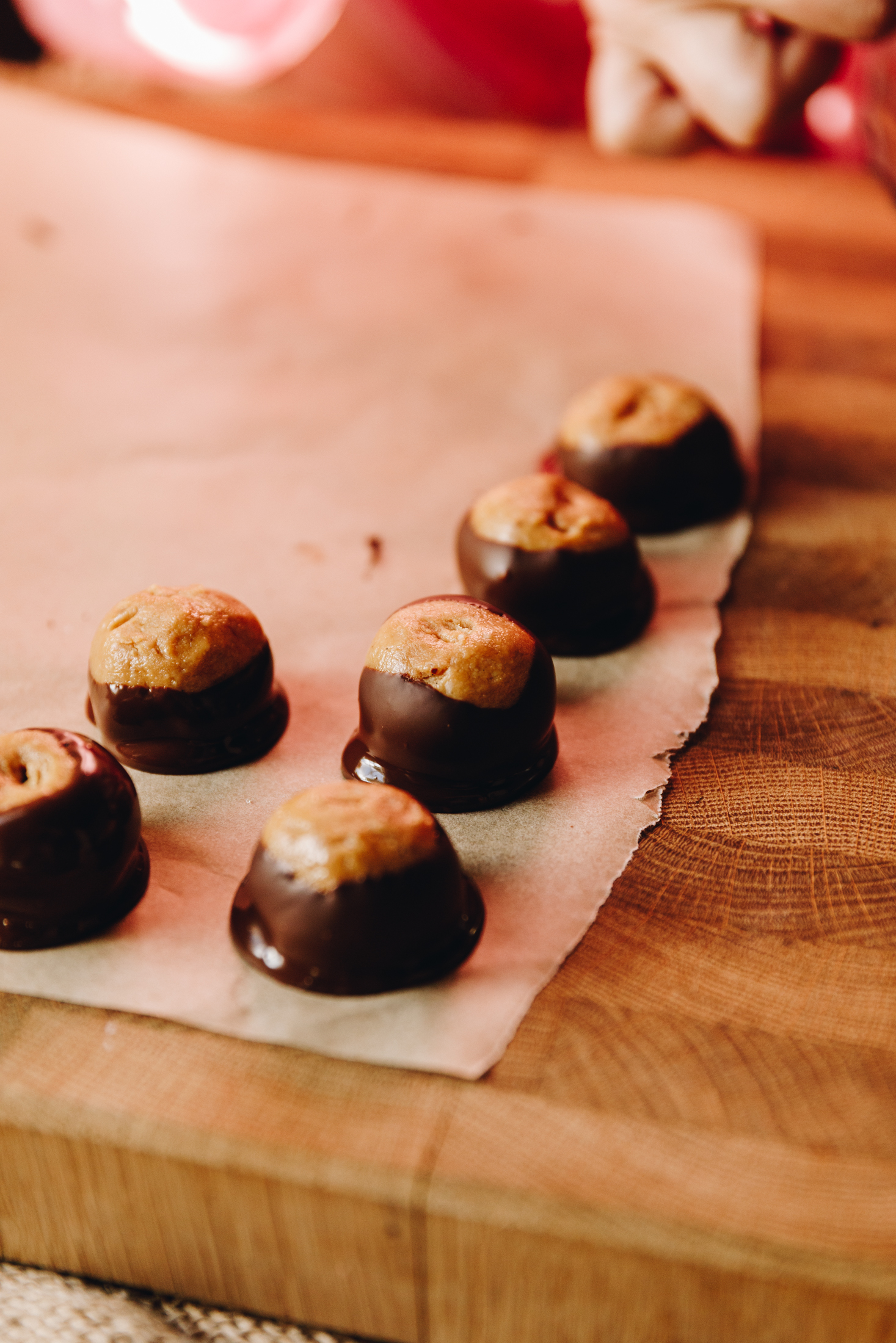 On a wooden board sits a large piece of baking paper with freshly dipped peanut butter buckeye truffles. 