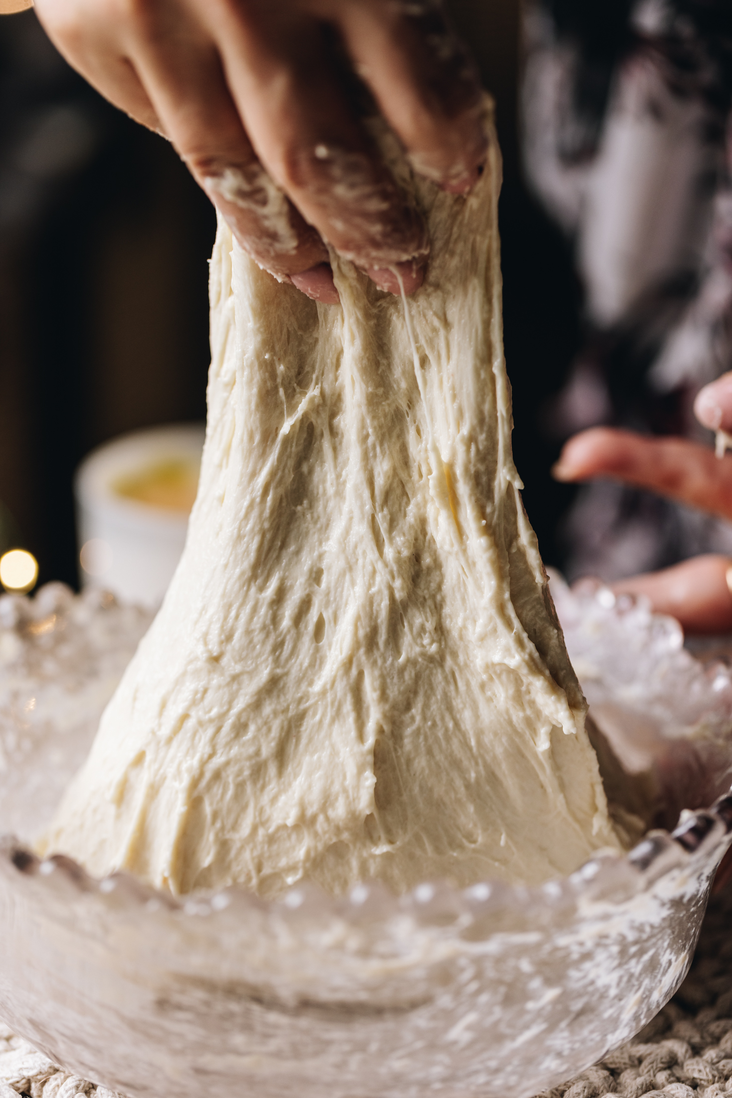 A hand is gathering the dough and stretching the dough. The dough is being lifted high in the air.