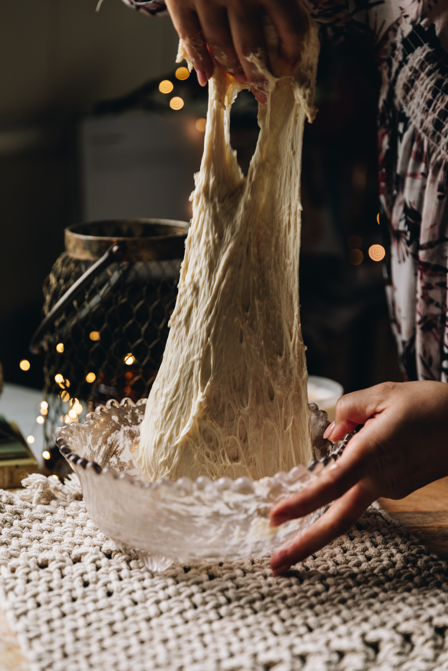 A hand is gathering the dough of the no-knead white bread loaf stretching the dough. The dough is being lifted high in the air.