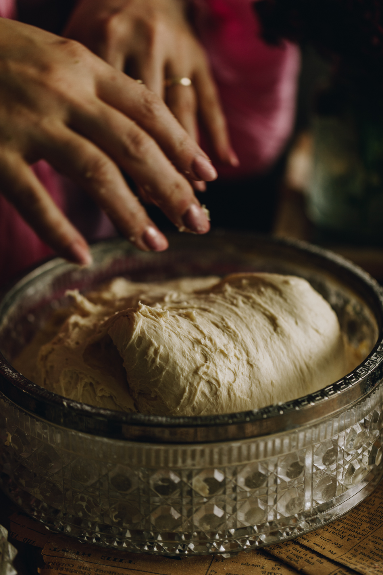 The dough is in a bowl, a hand is reaching in to grab it. 