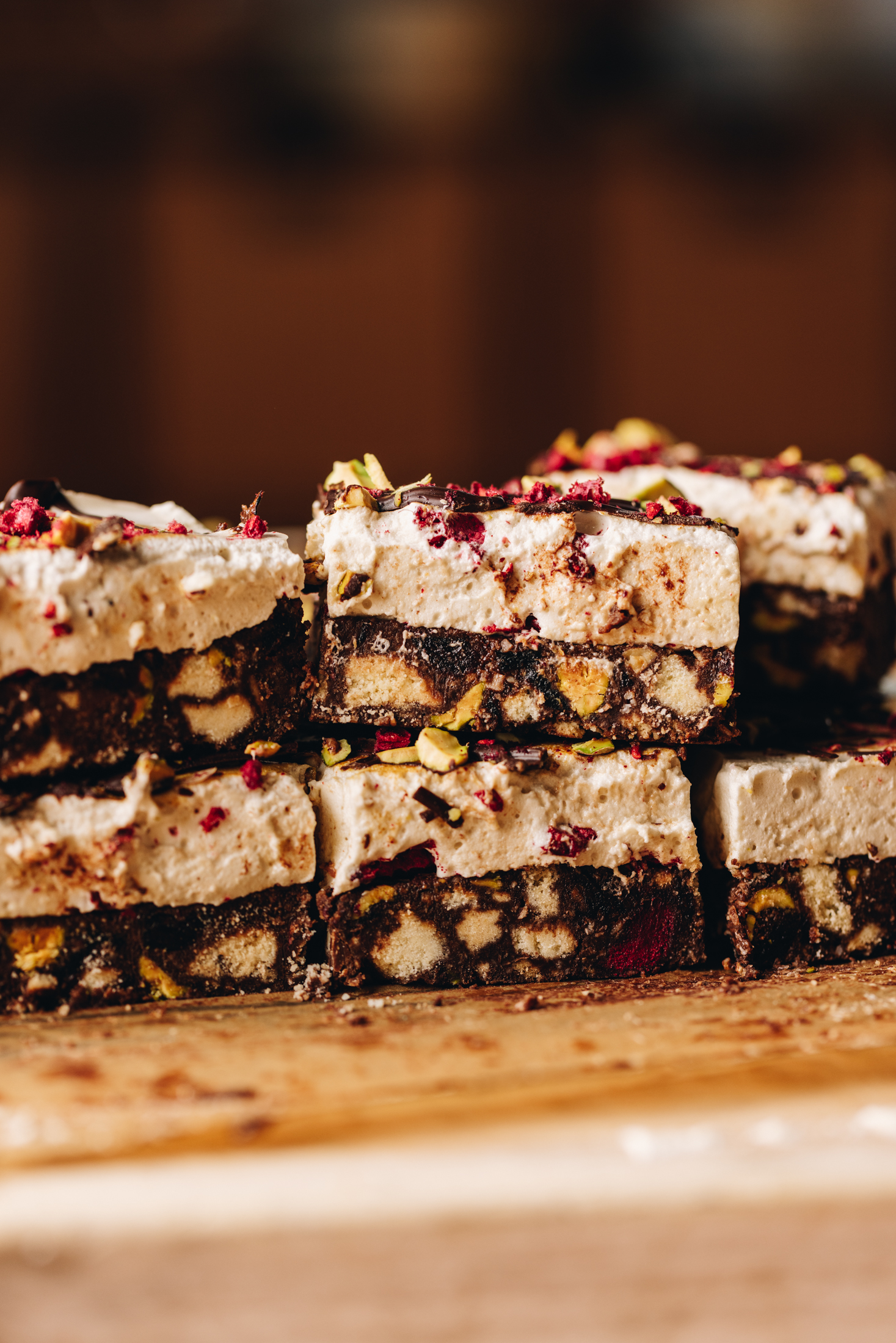 A wooden board sits on a wooden table. On top of the wooden board is pieces of no-bake marshmallow hedgehog slice. The pieces have been stacked on each other. 