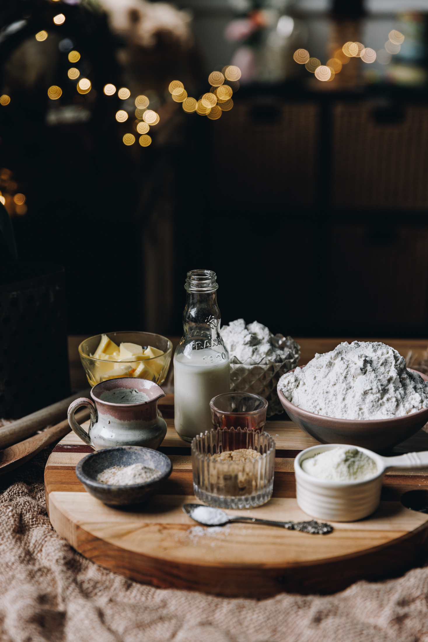 Chocolate Star Bread ingredients are in different vintage bowls and are sitting on a wooden board on top of wooden table. Fairy lights are in the background.