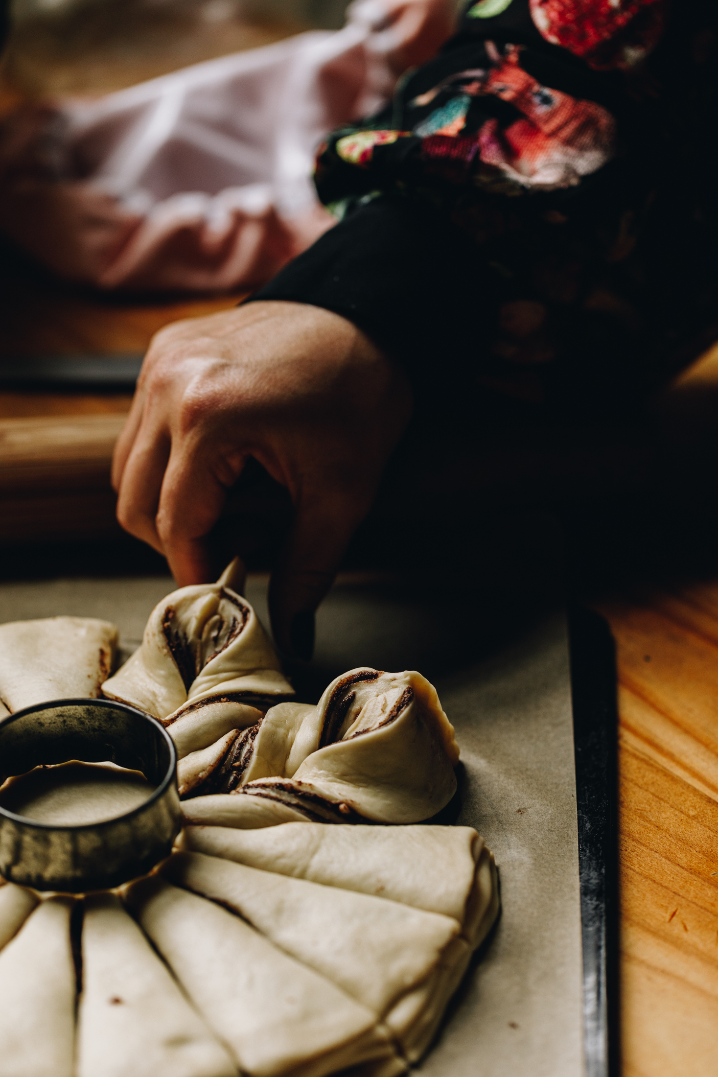 Unbaked Chocolate Star Bread is being twisted together to make the star shape. It is on a black tray with brown baking paper, It is on a wooden table.