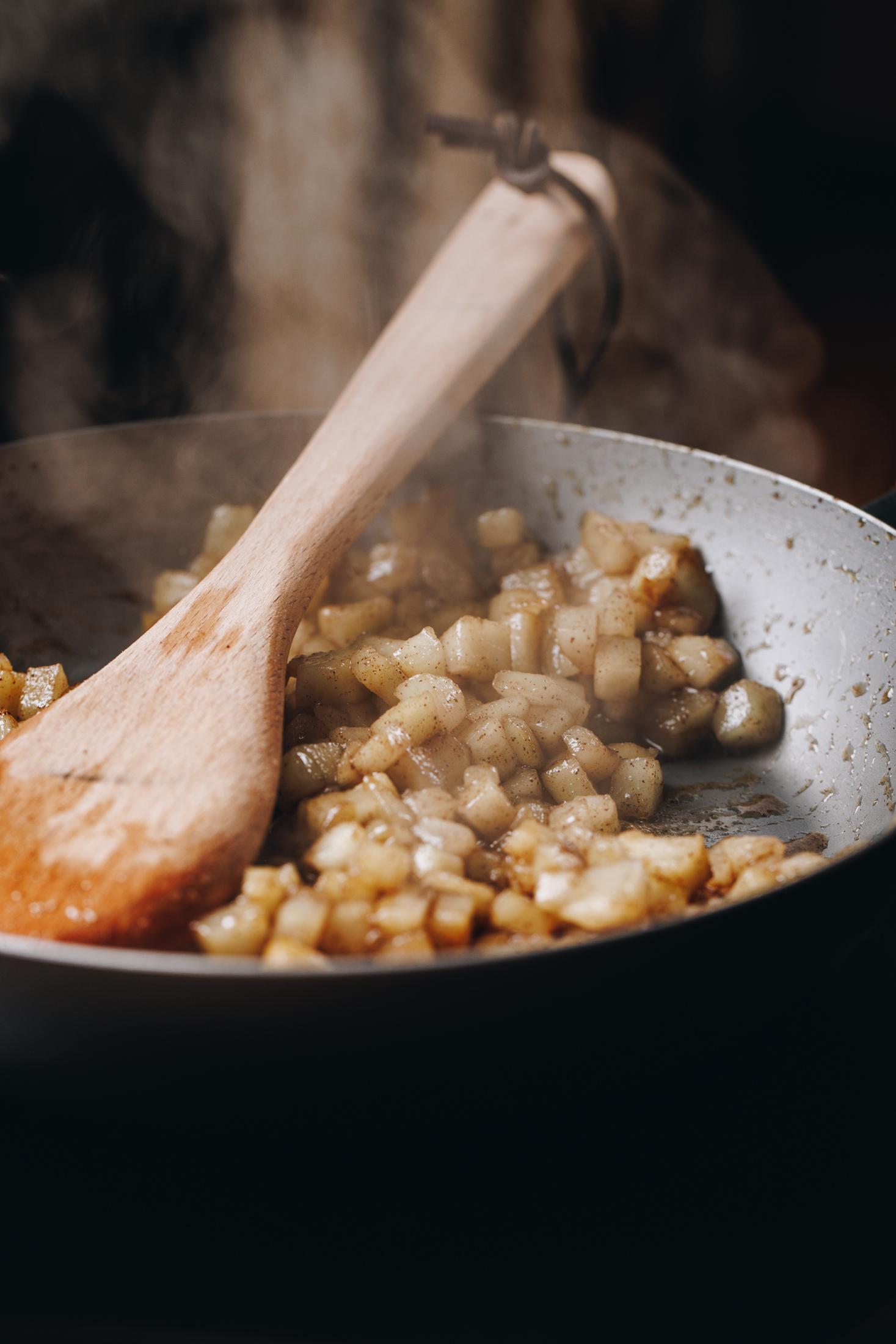 Easy spiced pear compote is cooking in a black cast iron pan. Steam is coming out of the compote and a wooden spoon is in the pan too.