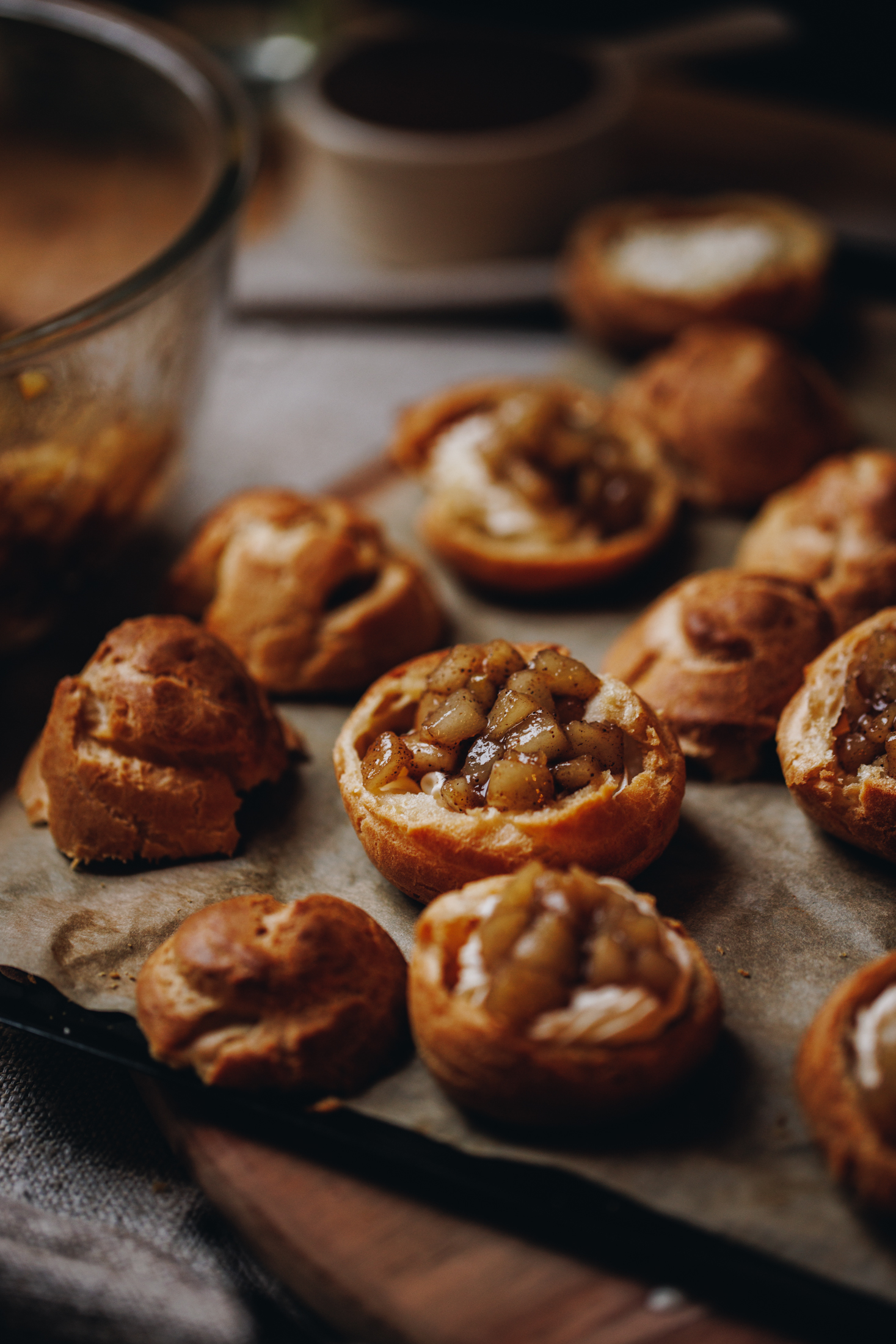 A black tray is lined with borne baking paper. On the paper is choux buns that have been filled with easy spiced pear compote. A bowl is next to it. 