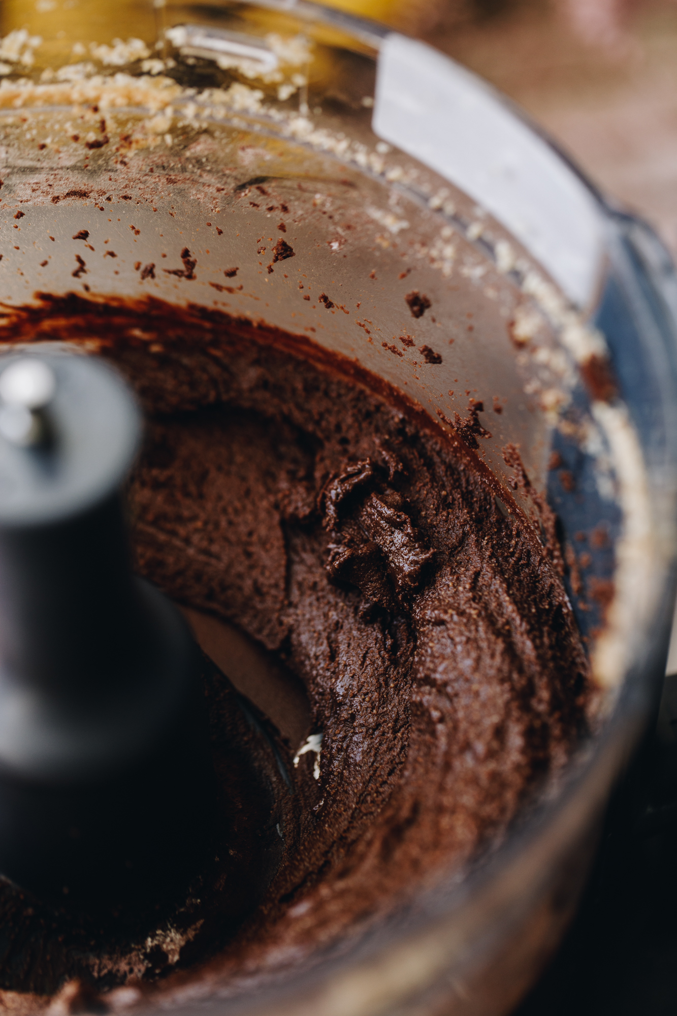 A close up shows chocolate almond butter whipped in a food processor. 