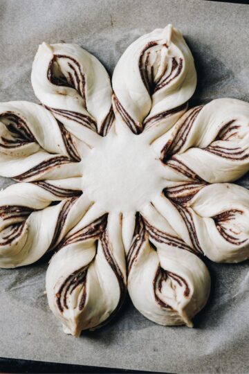 Flat lay shot reveals an unbaked star chocolate bread shaped in to a star on baking paper.