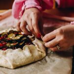 Hands are using the herbed shortcrust pastry to wrap the ingredients from the roasted tomato galette.