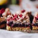 A close shot of one slice of Louise cake slice showing the buttery base, thick raspberry layer and coconut meringue with freeze dried raspberries on top.