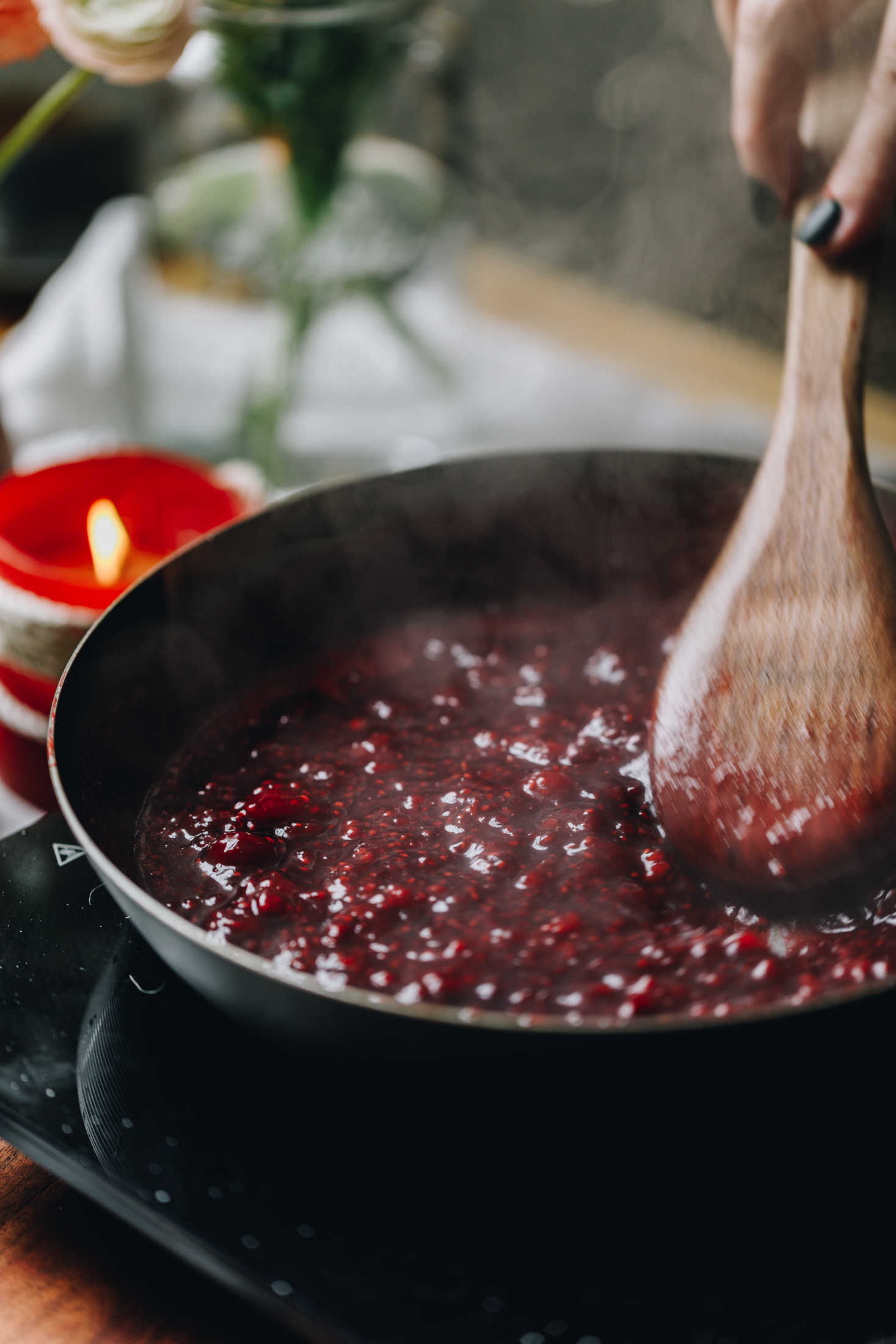 Chia raspberry and lemon jam is cooking over a black portable stove in a frying pan. The mixture is thick and steamy.