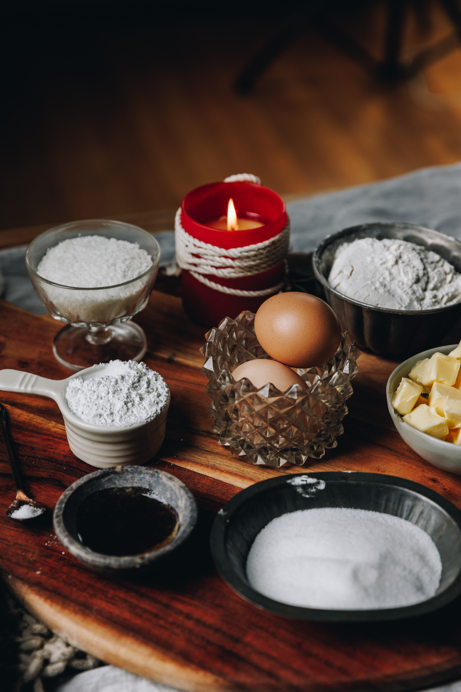 Louise Cake Slice ingredients are in different vintage bowls and are sitting on a wooden board. A red candle are behind the ingredients.