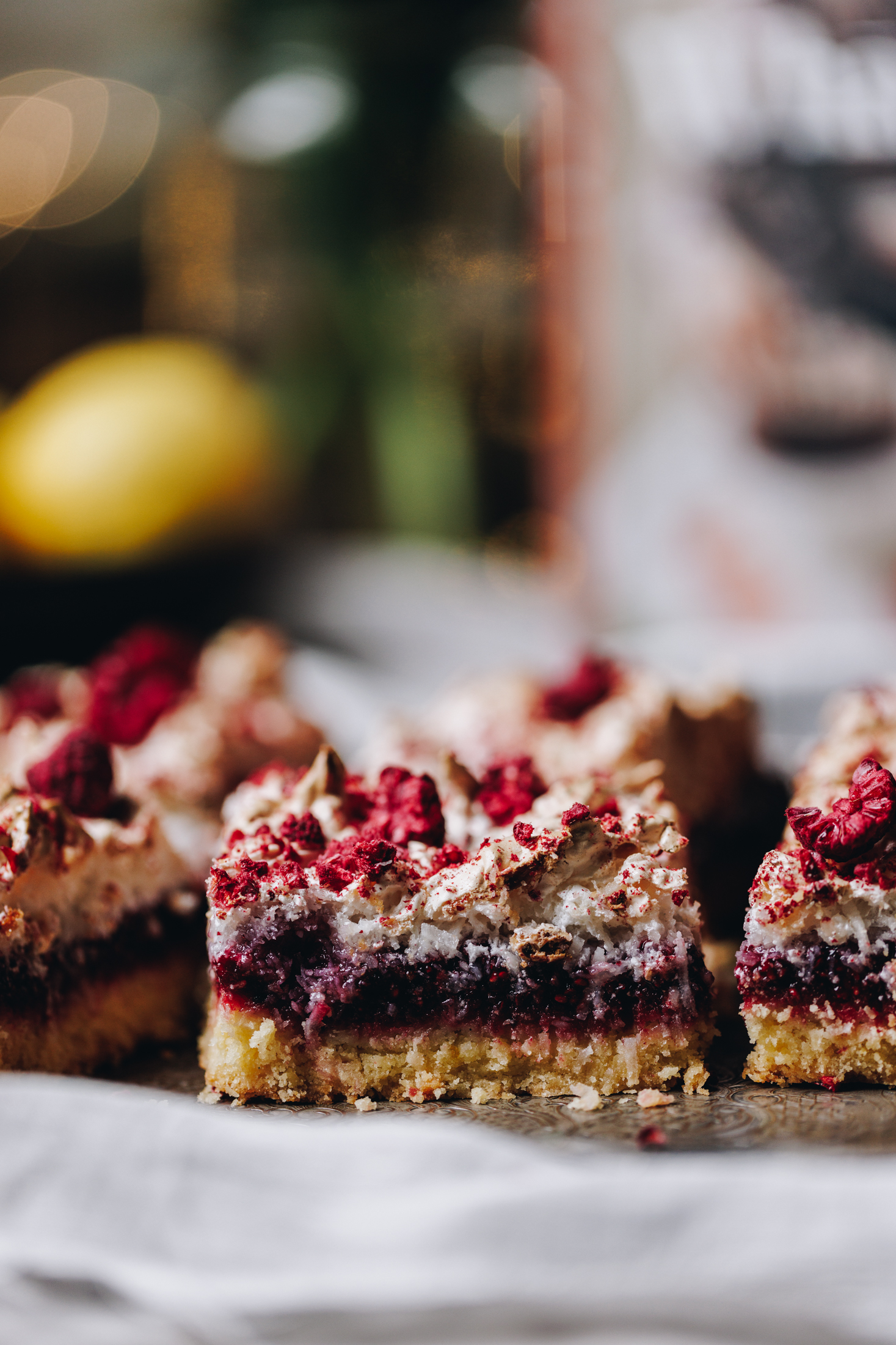 Close piece of Louise Cake Slice reveals the buttery base, thick raspberry slice and coconut meringue with free-dried raspberries.