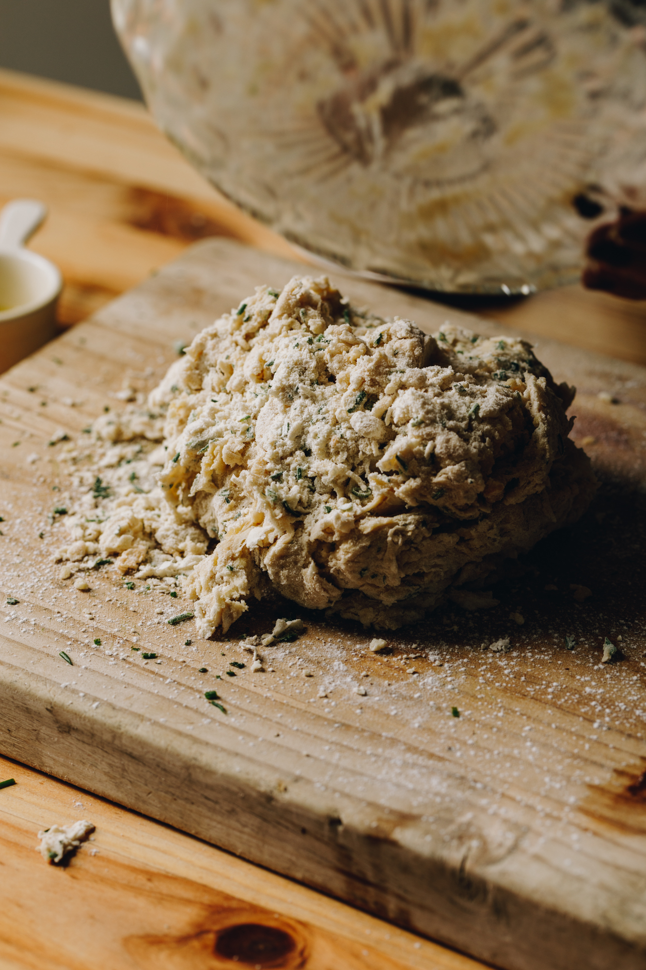 A wooden board sits on a wooden table. A vintage glass has just tipped out the bread dough on to the wooden board. A cream ceramic cups is in the background. 