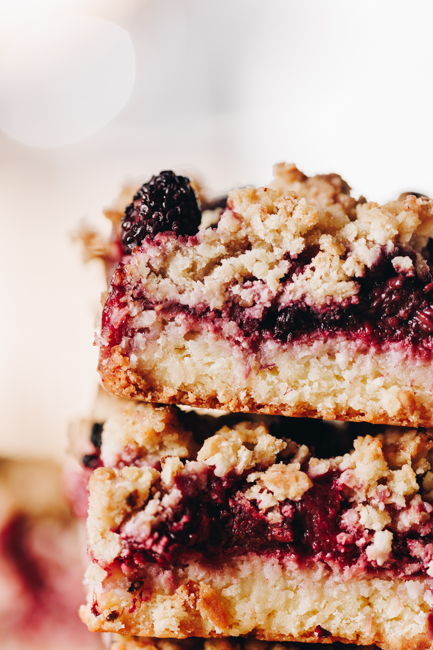 A close up shot shows two freshly baked berry oat crumble slices and the shot show the buttery base, the berry centre and the crumble topping of the slice.