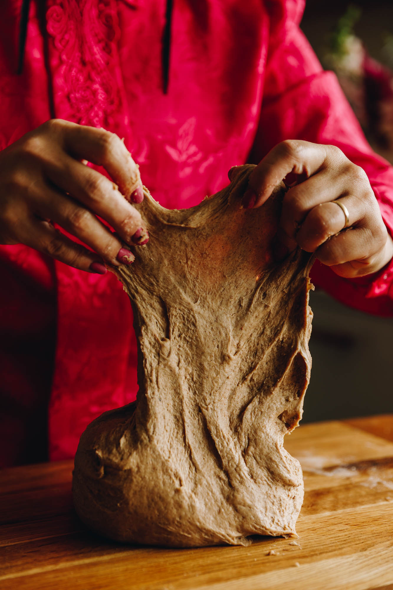 On a wooden table is a heavily spiced dough that is being lifted up to show the gluten stretch.