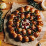 A whole baked brie cheese wreath is freshly baked and is sitting on a wooden board on baking paper. It is on a wooden table.