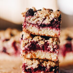 Three pieces of freshly baked berry oat crumble slice are piled on top of each other.
