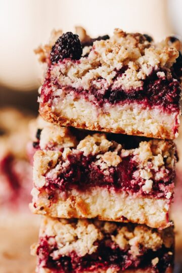 Three pieces of freshly baked berry oat crumble slice are piled on top of each other.