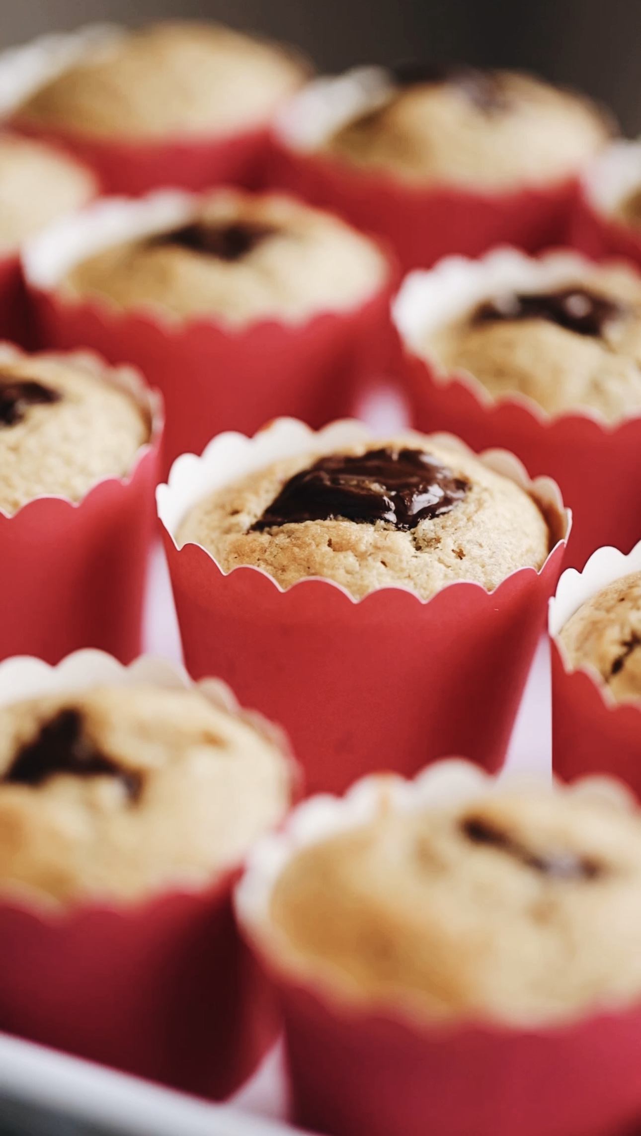 A whit stray has freshly baked simple banana cupcake on it. They are in pink cupcake cases and chocolate is in the centre.
