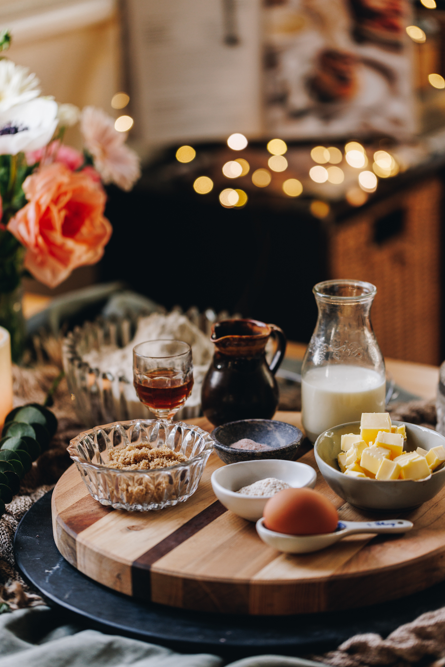On a wooden board sits vintage bowls and small plates that have dough ingredients on it. There is eggs, milk, butter and flour in view.