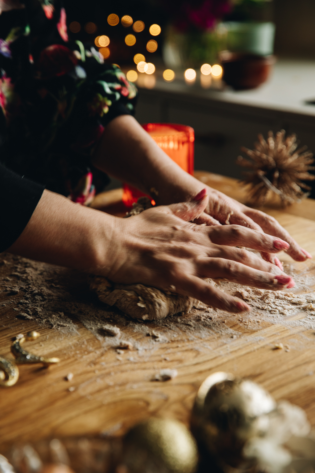 Naomi Toilalo is standing at a wooden table and is kneading dough. There is  fairy lights and an orange candle in the background.