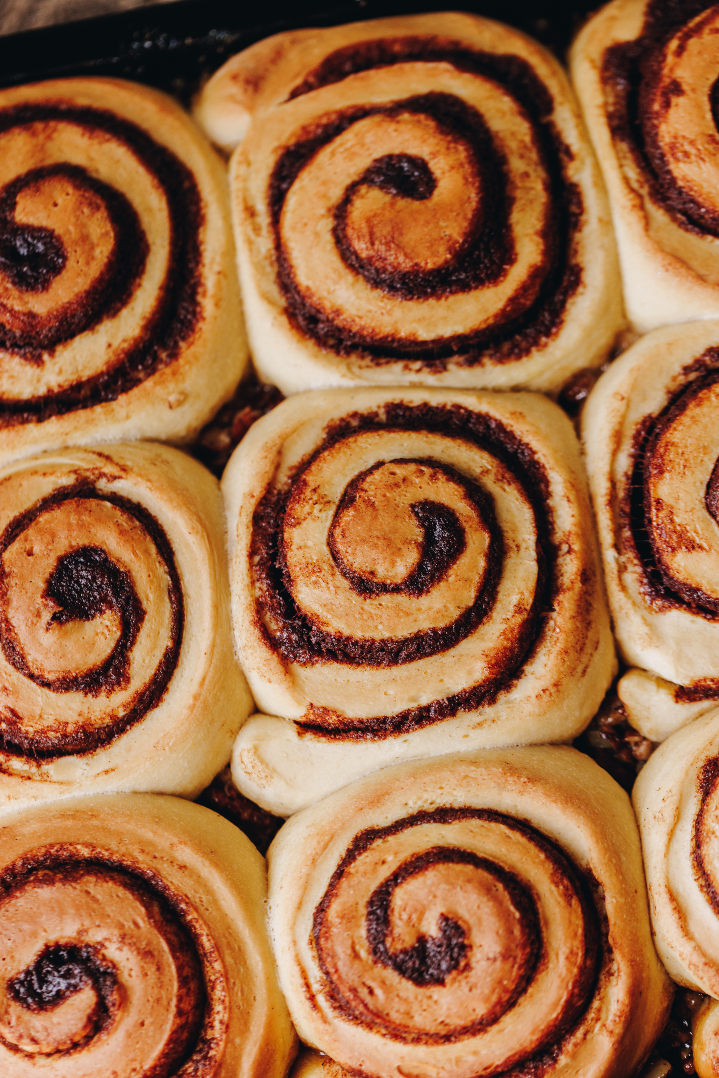 A flat lay shot shows a tray filled with baked sticky maple cinnamon scrolls. The dough has spirals of cinnamon butter in seen baked in to the dough but the caramel is not seen. The scrolls have not been flipped over yet. 