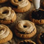 Peanut butter buttercream is being freshly piped on to ultimate peanut butter cookies, the swirl pattern is seen on every cookie.