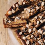 A flat lay shot shows the caramel and almond slice, one is sliced open and flipped on the side showing the biscuit base, caramel inside and almond chocolate crumble on top.