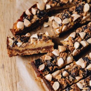 A flat lay shot shows the caramel and almond slice, one is sliced open and flipped on the side showing the biscuit base, caramel inside and almond chocolate crumble on top.
