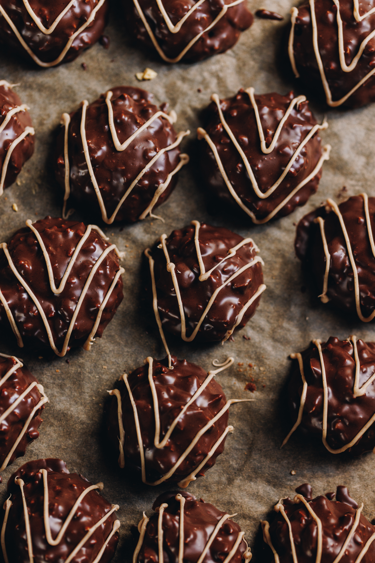 A top shot shows a tray line with brown baking paper with freshly dipped and decorated homemade squiggle top biscuits. They are dipped in dark chocolate and have a caramelised white chocolate squiggle on top of them.