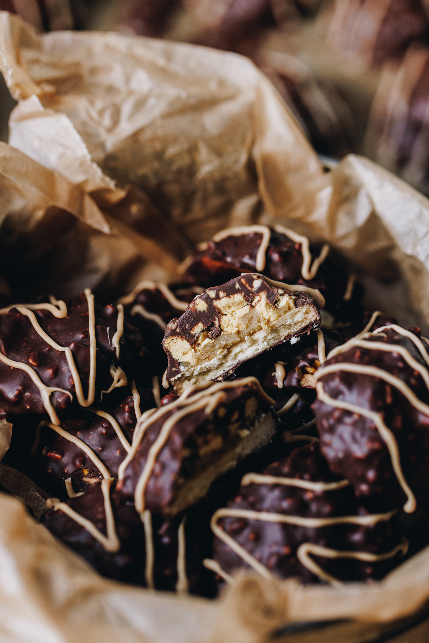 Decorated homemade squiggle top cookies are inside a cookie tin lined with baking paper. One of the cookies has been such open to reveal the layers of cookie, buttercream, hokeypokey and chocolate.