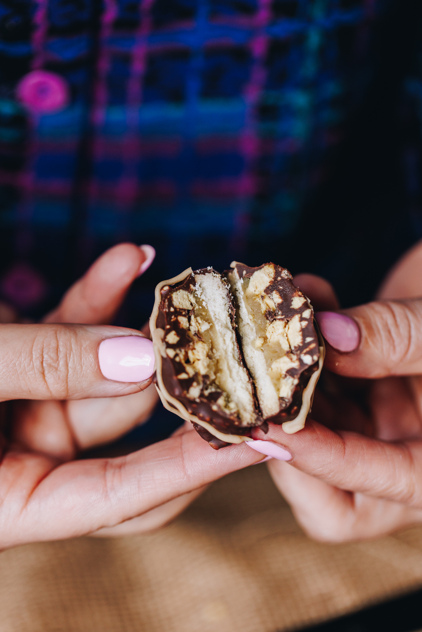 Naomi is holding a freshly baked homemade squiggle top biscuit in her hand. It has been cut open to reveal the layers of cookie, buttercream, hokey pokey and chocolate. It is a close shot.