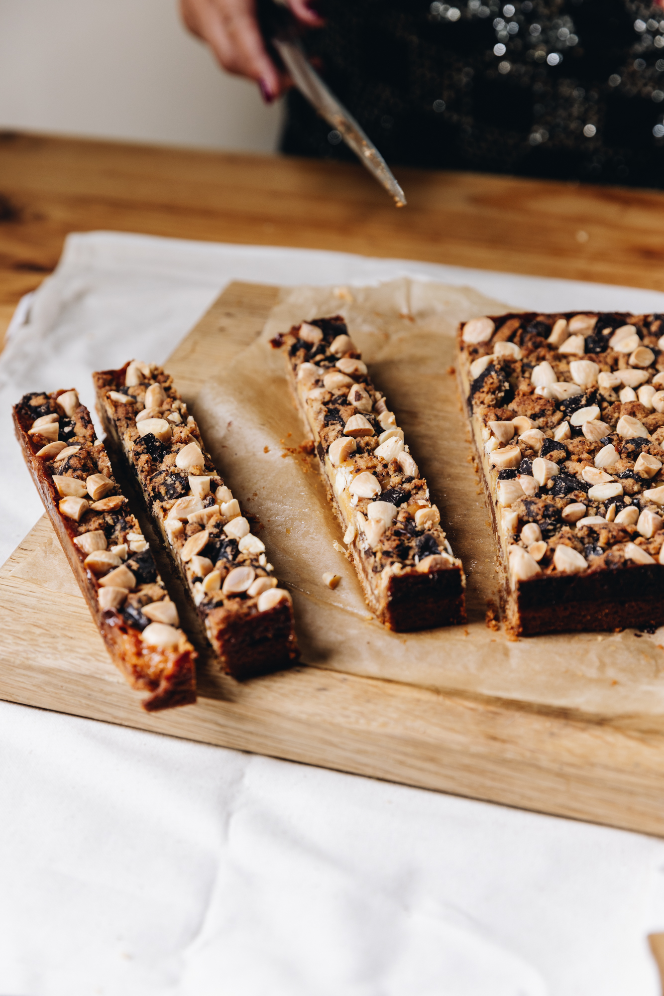 A wooden board sits on a cream table cloth, on a wooden table. On top is freshly baked slice that has been sliced in to long, thin slices.