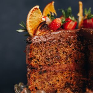 A close up shot of a kumara cake has been topped with dark chocolate buttercream, dried oranges and fresh strawberries.