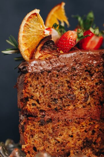 A close up shot of a kumara cake has been topped with dark chocolate buttercream, dried oranges and fresh strawberries.