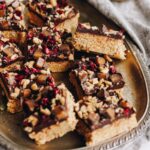 A sliver tray has sliced on toasted coconut fudge on it. The Fudge has been decorated with chocolate, caramel chocolates and free-dried boysenberries.