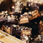 Caramel and almond chocolate bars are piled on top each of other, one is sliced open to reveal the inside of the bar showing the biscuit base, caramel inside and chocolate coating.