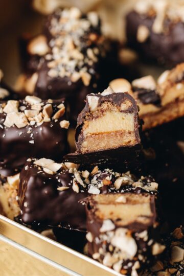 Caramel and almond chocolate bars are piled on top each of other, one is sliced open to reveal the inside of the bar showing the biscuit base, caramel inside and chocolate coating.