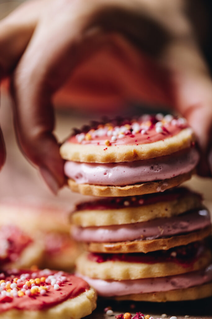 A hand is stacking hundreds and thousands biscuits that are filled with marshmallow. There is three in a pile. 